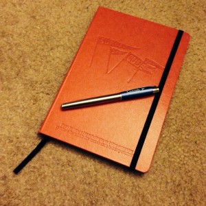 Red notebook and pen as part of the swag from GSoC Mentor Meetup 2013.